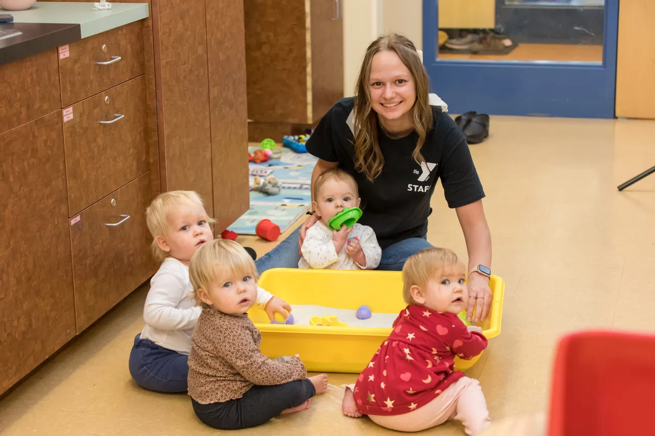 YMCA Child Care leader playing with infants in a small sandbox