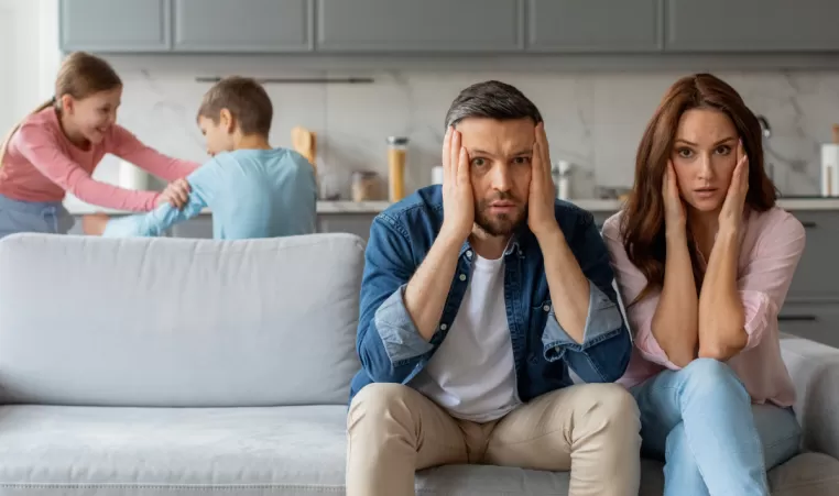 overwhelmed parents with kids play fighting in the background