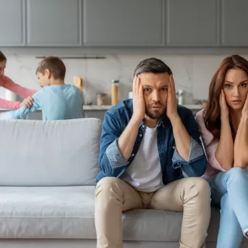 overwhelmed parents with kids play fighting in the background